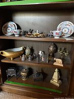 Display of various Staffordshire teacup sets, Victorian trinket dishes, and Roman-style figurines arranged on wooden shelves.
