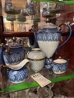 Set of 2 blue and white porcelain teapots, white vase with gold lattice, creamer, and sugar bowl displayed in cabinet.