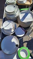 Photo showing multiple stacks of white ceramic plates with some small parts of colored airline logos visible, all plates appear vintage with some gold trim.