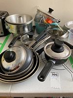 Photo of assorted metal pots, frying pans with lids, glass lid, and Bundt cake pan stacked on counter