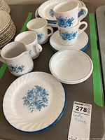 Several stacked dinner plates and cups with blue floral design on Corelle dishes. Includes plates, cups, and small bowls.