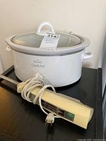 Rival Crock-Pot slow cooker with glass lid. Sunbeam electric carver with cream handle and cord in front.