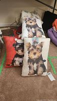 Three decorative dog cushions stacked on floor, showing realistic Yorkshire Terrier images, and blankets behind them