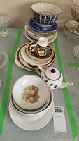 Stack of assorted plates with varied decorative patterns, teapot, and Royal Albert teacup and saucer on top.