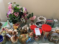 Overview of lot showing faux flower arrangement, dog figurines, tin cans, and porcelain flowers.