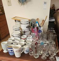 Full view of all glasswares, coffee mugs, airtight containers, and utensils on wooden table.