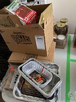 Box containing various foil baking pans of different sizes stacked together, along with a partially visible box containing other items.