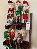 Photo showing six assorted nutcracker figurines arranged in two rows including two Santa designs, a green soldier, a snowman, and two traditional nutcrackers.