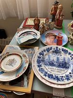 Commemorative plates featuring Diana, Queen Elizabeth II, Queen Mum, and Canada Centennial plate with several figurines and books.