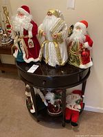 Six Santa Claus figures displayed on and around a half-circle wooden table, showing different poses and outfits.