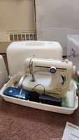 White Euro-Pro X model 464XC sewing machine placed in carrying case, showing front and base with accessories.