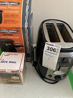 Black & Decker stainless steel 2-slot toaster with power cord coiled next to it. Proctor Silex boxed electric can opener and boxed Magic Grater set behind and next to the toaster.