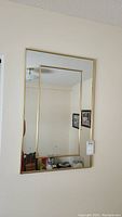 Front view of rectangular wall mirror with gold tone metal frame and inset smaller rectangular mirror hanging on a wall.