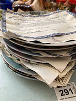 Stack of collector plates with papers, Certificates of Authenticity visible on top