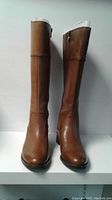 Front view of pair of brown leather tall boots with rounded toes and low block heels, standing upright.