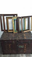 Six antique wooden picture frames of varying sizes with natural and teal finishes, placed leaning against a rustic trunk.
