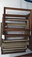Six wooden antique picture frames stacked against a wall, varying in finish and design.