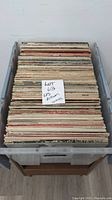 Top-down view of 12 vinyl LP albums packed vertically in a plastic container, showing album spines and edges.