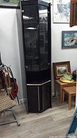 Full view of the black lacquer display cabinet showing its tall, narrow shape with glass in the upper section and solid doors below with gold trim.