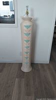 Full view of the tall beige chalk floor lamp with turquoise geometric arrows on front, showing condition and shape.
