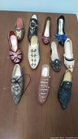 Photo of 11 women's mini collectible shoes in various styles and decorations arranged on a wooden surface.