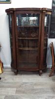 Front view of curved glass wooden display cabinet showing three shelves and door with veneer damage.