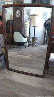 Full view of large rectangular wood-framed mid-century wall mirror resting on floor showing general shape and frame style