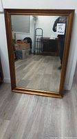 Full front view of the large wall mirror showing its rectangular shape, gold frame and reflective surface showing room reflection.