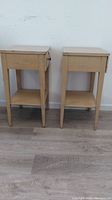 Pair of wooden MENGEL nightstands with light natural finish, each with single drawer and open shelf. Shows marks and dirt indicating need for cleaning.
