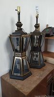Pair of vintage mid-century Spanish style table lamps side by side on wooden surface, one with 6 candle holders, one with a single bulb base.