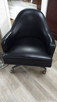 Front view of black leather or leather-like mid-century swivel chair with curved back and armrests.