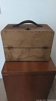 Closed wooden case with leather handle on top showing wear and water stains.