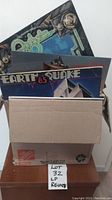 Photo of a cardboard box packed with LP vinyl albums including Earthquake album visible on top.