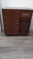 Full view of the closed vintage wooden radio cabinet showing front speaker grille with decorative pattern, control knobs, and frequency dial.