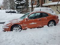 Left side view of snow-covered orange coupe
