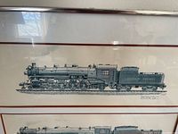 Close-up photo of one framed artwork showing detailed line-drawing of a Canadian Pacific steam locomotive with text identifying it as Mountain Type 4-6-2 CPR Class T-1-a.