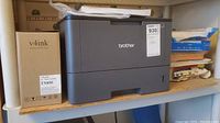 Brother printer on shelf with toner box and loaded paper on top