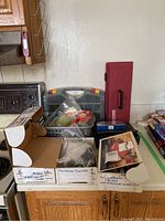 View of boxes containing nails, hooks, felt pads and other furniture supplies on a kitchen counter.