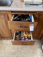 View of the two wooden drawers open, filled with mixed cutlery and kitchen utensils, with some packaging on counter above.