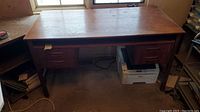 Front view of mid-century modern desk with four drawers, showing the full top surface and legs, with visible wear and various items around it.