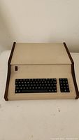 Front view of microcomputer showing beige chassis, walnut wood end cheeks, chiclet keyboard, numeric keypad and red power switch