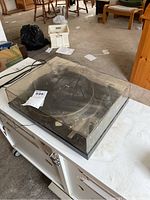 Dust-covered turntable in closed dust cover on white cabinet