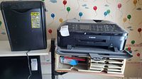 Photo showing black Amazon Basics shredder next to Canon MX922 printer with drawers and paper below, colorful balloon wallpaper background