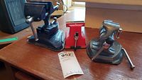 Photo of all three table top vises on wooden surface, showing overall size and colors (metallic gray and red). Includes MaxSold tag.