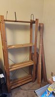Front view of assembled wood shelving unit with 4 shelves next to disassembled wood shelving parts leaning against the wall.