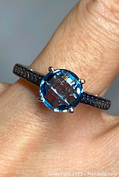 Close-up of ring on finger showing large round blue topaz stone and smaller blue diamonds on band.