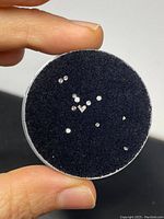 Close-up of small 1mm diamonds placed on a black foam inside a round transparent container held between fingers.