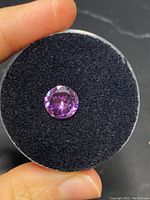 Close-up photo of a loose round amethyst stone holding on black foam background, showing the purple faceted gemstone.