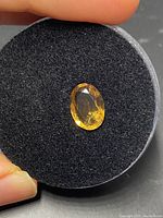 Close-up image of the loose oval citrine gemstone on a black foam-like holder showing color, cut, and facets.