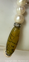 Close-up of the yellow decorative bead with black veining and rhinestone accents between pearl beads.